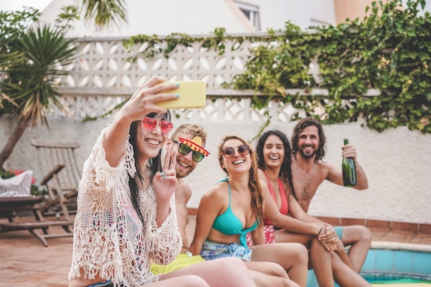 Amigos loucos felizes se divertindo tirando uma selfie e sentando ao lado da piscina -