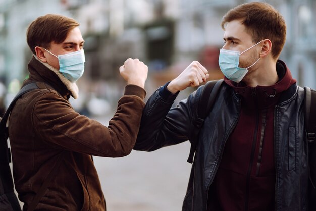 Amigos en máscara médica protectora en su rostro saludan a sus codos