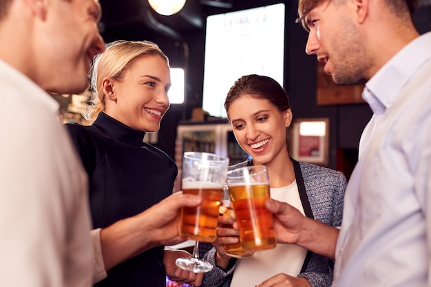 Amigos masculinos y femeninos haciendo un brindis mientras se reúnen para tomar una copa y socializar en el bar después del trabajo