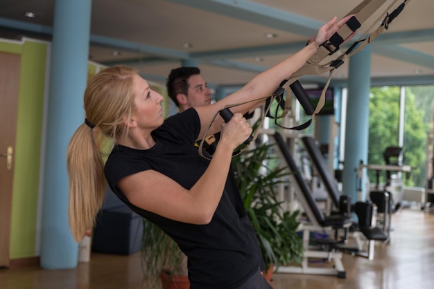 Amigos masculinos y femeninos trabajando con Trx en el gimnasio