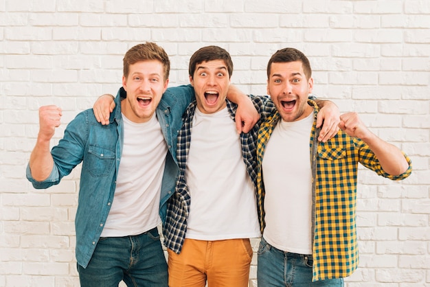 Foto amigos masculinos jovenes emocionados que se oponen a la pared blanca que aprieta su puño