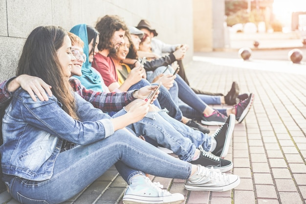 Amigos milenarios que usan teléfonos inteligentes sentados al aire libre