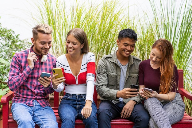 Amigos multiculturais se divertindo juntos olhando seus smartphones no jardim dehor no campus da faculdade Pessoas viciadas em telefones inteligentes móveis Conceito de tecnologia com millenials sempre conectados