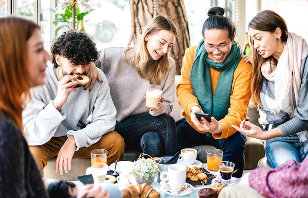 Amigos multiculturales jugando con teléfono móvil en la cafetería.