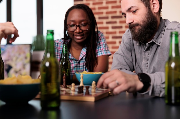 Retrato de homem afro-americano pensando em estratégia de jogo em jogos de  cartas com amigos, se divertindo na sala de estar. jovem adulto desfrutando  de jogo de tabuleiro com táticas, bebendo cerveja
