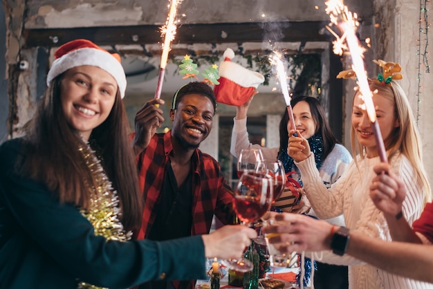 Amigos multiétnicos brindando vino. Hombres y mujeres jóvenes que tienen una fiesta en la cafetería. Navidad.