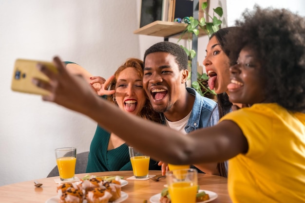 Amigos multiétnicos en un desayuno con jugo de naranja y muffins en casa selfie sonriendo y divirtiéndose