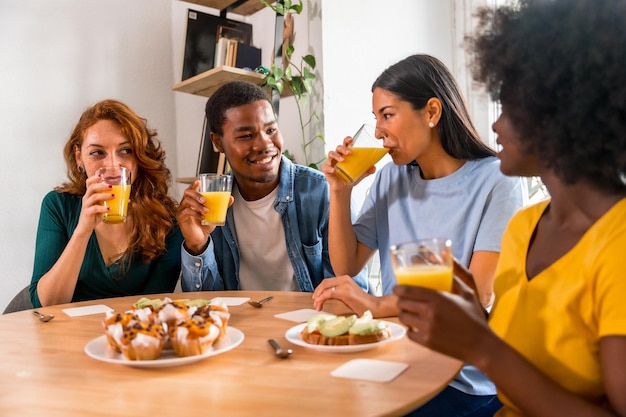 Amigos multiétnicos divirtiéndose en un desayuno con jugo de naranja y muffins en casa