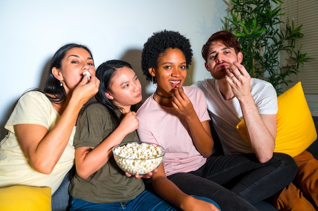Amigos multiétnicos numa noite de cinema em casa com pipoca