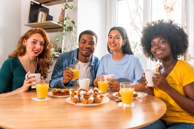 Foto amigos multiétnicos tomando café da manhã com suco de laranja e muffins em casa