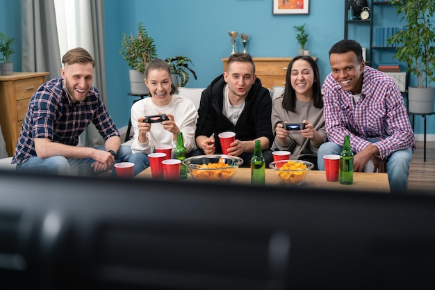 Amigos multinacionais sentados em casa no sofá e jogando videogame no console