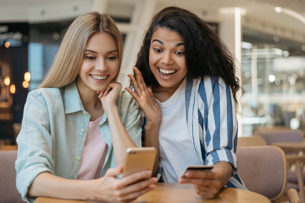 Amigos multirraciais felizes comprando online com grandes promoções, sentados à mesa juntos