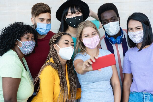 Foto amigos multirraciais tirando uma selfie usando máscaras ao ar livre