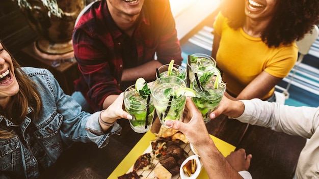 Amigos multirraciais torcendo por mojitos no bar restaurante