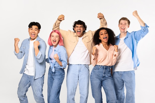 Amigos multirraciales adolescentes llenos de alegría gritando y agitando los puños posando mirando a la cámara de pie