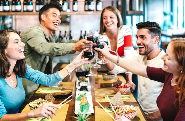 Foto amigos multirraciales brindando vino tinto en el restaurante de sushi