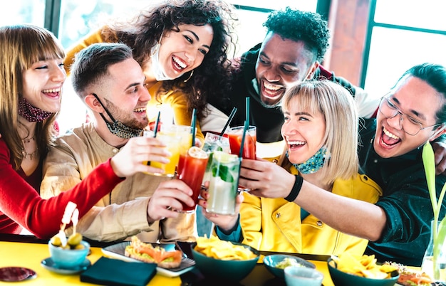 Amigos multirraciales felices brindando bebidas con máscaras faciales abiertas