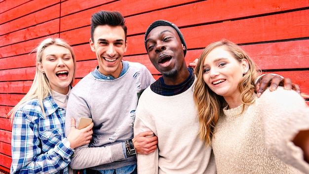 Amigos multirraciales felices tomando selfie de grupo en el fondo de madera roja