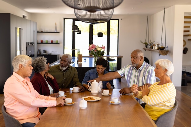 Amigos multirraciales mayores hablando y disfrutando de un café con galletas en la mesa del comedor en un asilo de ancianos. Meriendas, bebida, comida, inalterable, amistad, unión, apoyo, vida asistida, jubilación.