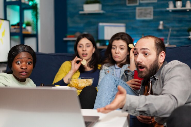Foto amigos multirraciales que se relajan en el sofá mientras ven la comedia con cara de sorpresa durante la noche de cine. grupo de personas multiétnicas que pasan tiempo juntos bebiendo cerveza, comiendo bocadillos a altas horas de la noche.