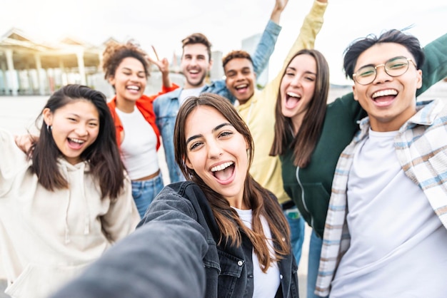 Amigos multirraciales tomando una foto de grupo selfie con un teléfono móvil inteligente afuera en la calle de la ciudad