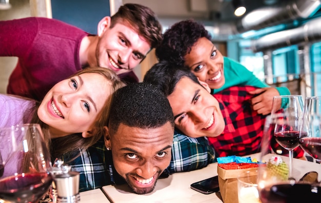 Amigos multirraciales tomando selfie borracho en el restaurante de la bodega de lujo