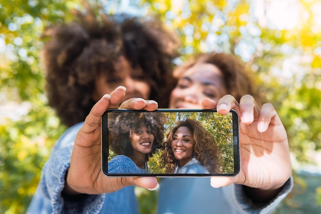 Amigos negros afro alegres em um humor divertido tirando selfie com smartphone usando a câmera frontal