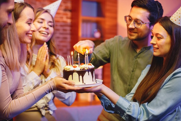 Amigos parados juntos sosteniendo un plato con un pastel y celebrando un cumpleaños