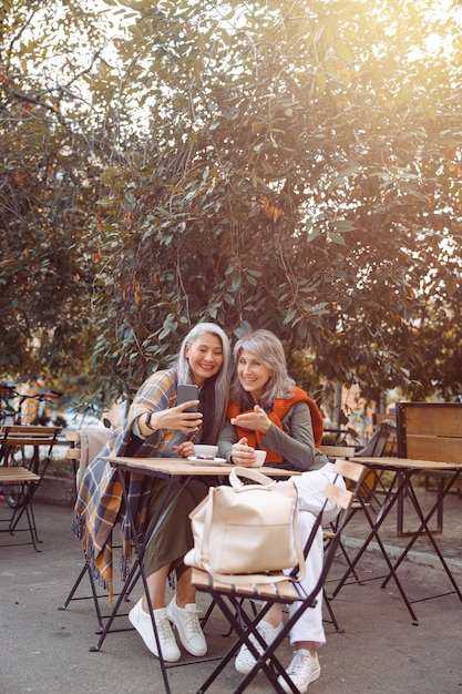 Amigos de pelo gris felices hablan en videochat sentados en una mesa pequeña en el café