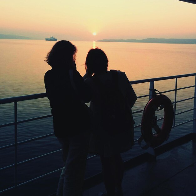 Foto amigos de pie en la pasarela junto al mar al atardecer