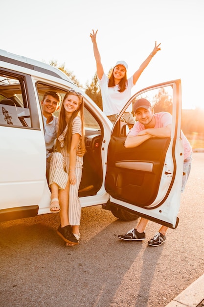 Amigos posando cerca del coche en el concepto de viaje por carretera al atardecer