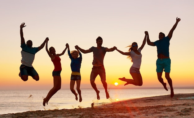 Amigos pulando na praia à beira-mar ao pôr do sol