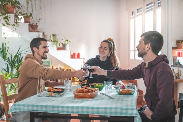 Amigos que se divierten durante la cena en la mesa del comedor en casa Alegre comiendo tostado y disfrutando