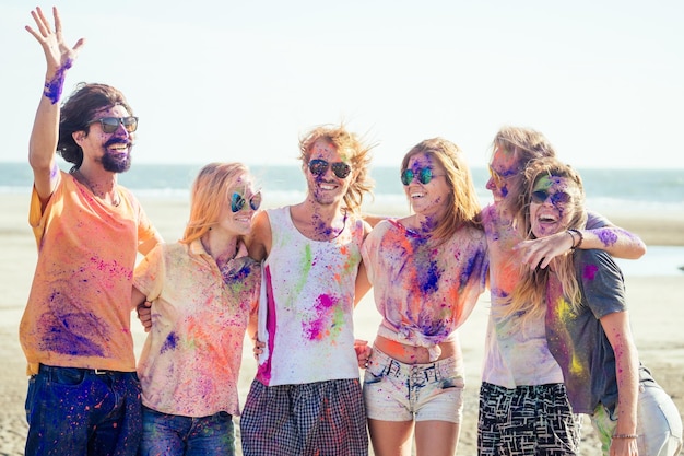 Amigos de raza mixta divirtiéndose con colores en la playa al aire libre en Goa, India