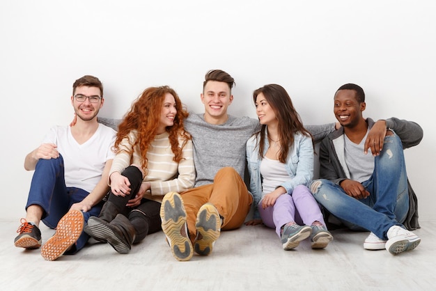 Amigos riendo felices, estudiantes diversos en casual juntos en el interior. Fondo blanco, espacio de copia