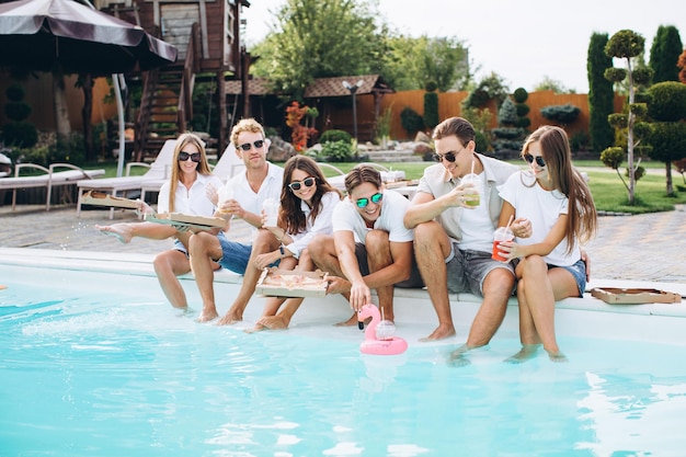 Amigos saindo à beira da piscina Eles comem pizza bebem coquetéis e se divertem