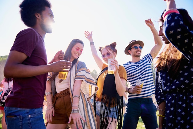Amigos segurando bebidas em copos enquanto dançam contra o céu