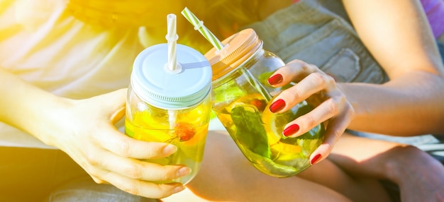 Amigos segurando limonada fresca em potes com canudos. festa de verão hipster com bebidas. estilo de vida vegano saudável. eco-friendly na natureza. limões, laranjas e bagas com hortelã no copo.