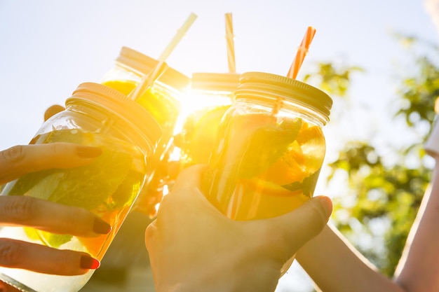 Amigos segurando limonada fresca em uma jarra com canudo. festa de verão hipster com bebidas. estilo de vida vegano saudável. eco-friendly na natureza. limões, laranjas e bagas com hortelã no copo.