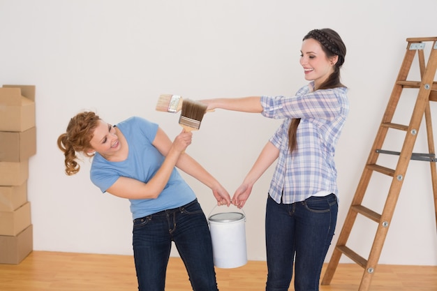 Amigos segurando pincéis e podem em uma nova casa