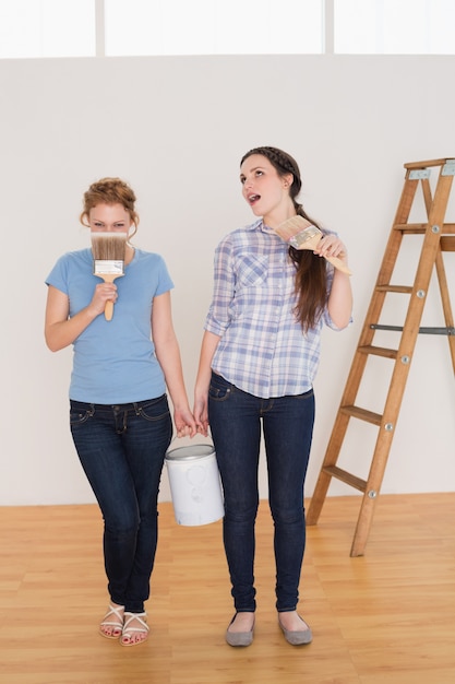 Amigos segurando pincéis e podem em uma nova casa