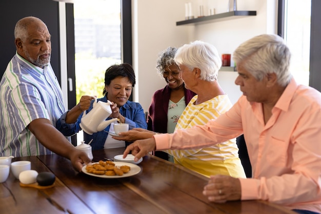 Amigos seniores multirraciais felizes desfrutando de café e biscoitos em casa de repouso. Lanches, bebidas, comida, inalterados, amizade, união, apoio, vida assistida e aposentadoria.