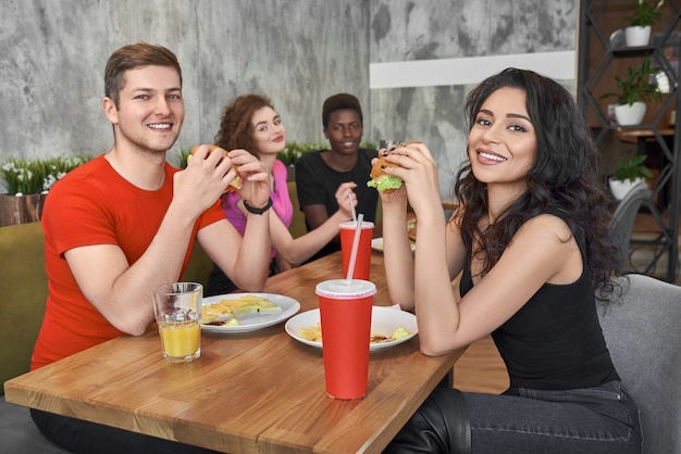 Foto amigos sentados en la cafetería de comida rápida, comiendo hamburguesas.