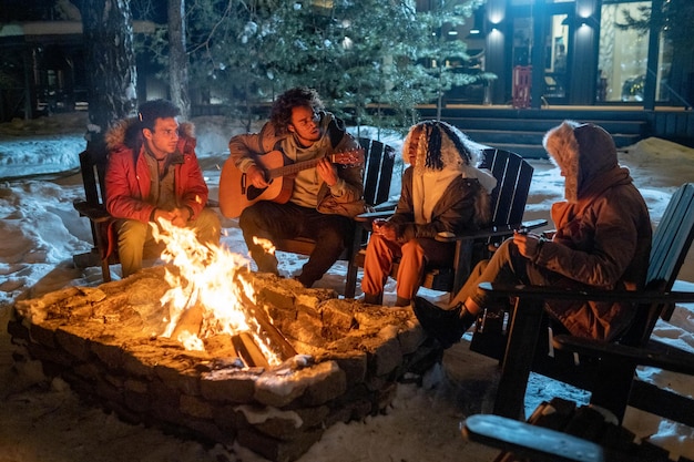 Amigos sentados cerca del fuego al aire libre en la noche de invierno