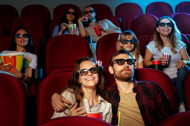 Amigos sentados en el cine ven una película comiendo palomitas y bebiendo agua.