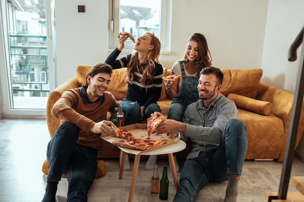 Foto amigos sentados na sala e comendo pizza