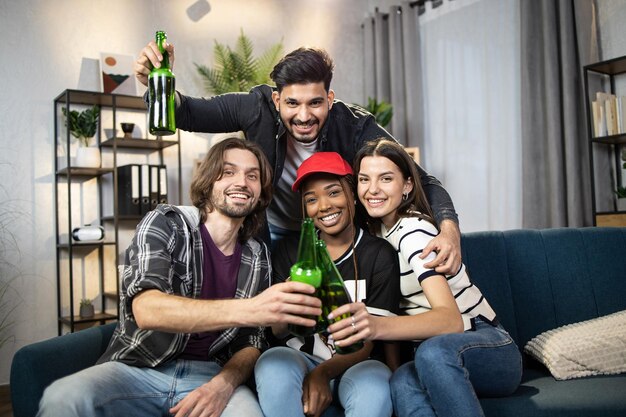 Amigos sentados en el sofá con cerveza y sonriendo a la cámara