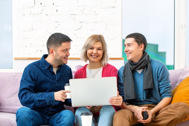 Amigos sentam no sofá conversando e usando um laptop de computador desktop smartphone