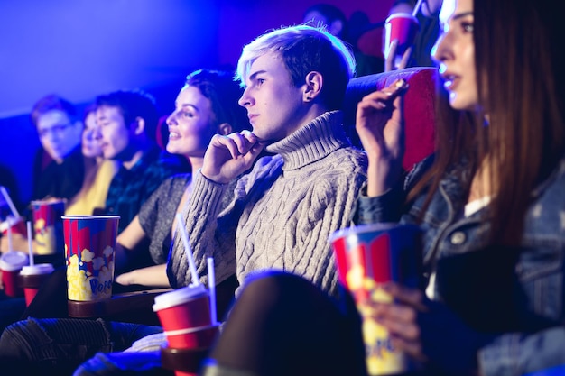 Los amigos se sientan y comen palomitas de maíz juntos mientras ven películas en una sala de cine