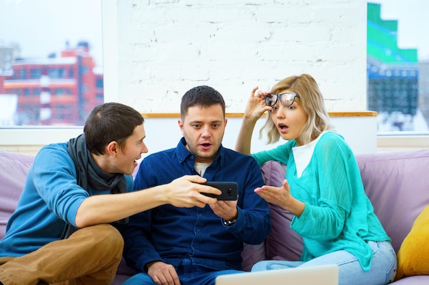 Los amigos se sientan en el sofá charlando y usando una computadora portátil de escritorio con teléfono inteligente